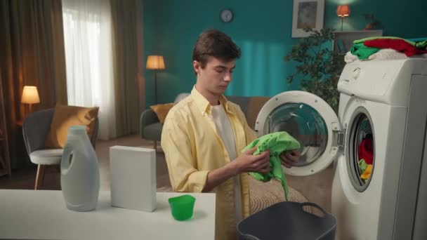 黑头发男子站在洗衣机旁边 卸下洗不掉的衣服 用洗涤剂看了看盒子 对结果感到沮丧 家用电器 家务活 — 图库视频影像