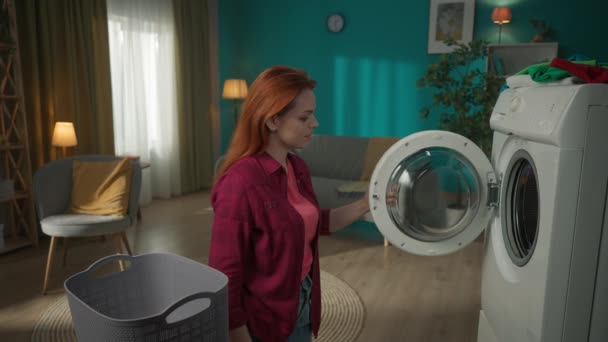 红头发的女人站在洗衣机旁边卸下它 衣服湿透了 女人强调机器没有完成烘干 家用电器 家务活 — 图库视频影像