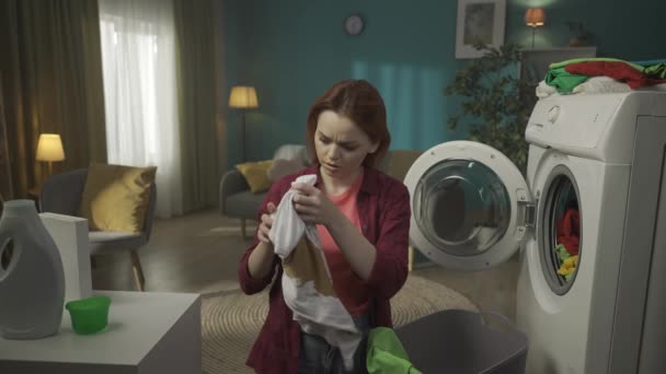 红头发的女人站在洗衣机旁边 卸下洗不掉的衣服 在相机前展示一件污迹斑斑的T恤 摇着头 家用电器 Hdr — 图库视频影像
