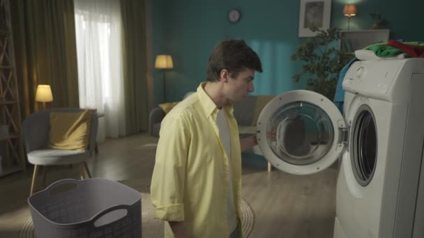 Mörkhårig Man Som Står Bredvid Tvättmaskin Och Lastar Den Kläderna — Stockvideo