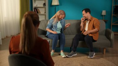 A married couple laughs while recalling funny moments from life at the psychotherapists appointment. Spouses sitting on the couch in the office in front of a family relationship expert. clipart