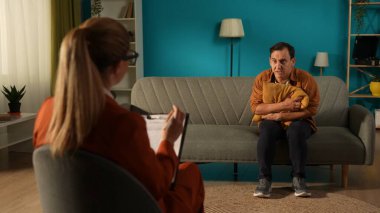 Depresyondan muzdarip mutsuz bir adamla çalışan bir kadın psikolog. Bir adam bir uzmanın önünde kanepede oturuyor, yastığa sarılıyor. Ruh sağlığı, depresyon, panik atak kavramı