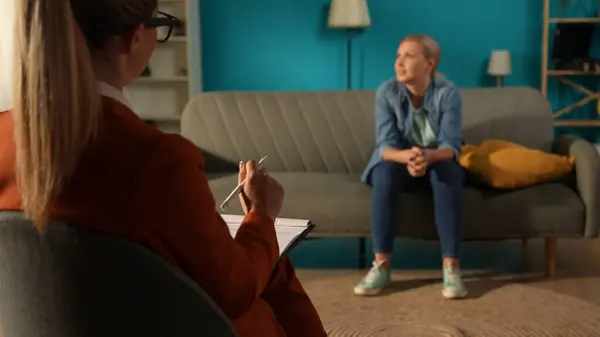 A woman sitting on a couch in a psychotherapy session. A female psychologist trying to help her solve her problems. Concept of mental health therapy