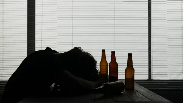 カフェのテーブルに座っている若者のシルエット 近くにはアルコールの空きボトルがあります 彼はアルコール中毒を示しているので 彼はテーブルで眠った 孤独で依存している — ストック写真
