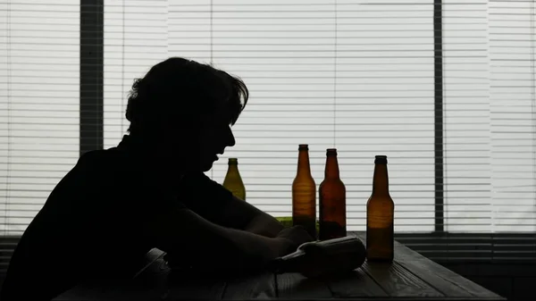 カフェのテーブルに座っている若者のシルエット 近くにはアルコールの空きボトルがあります 彼は一人で座っているアルコール中毒を示し 彼は悲しみ 中毒です ミディアムショット — ストック写真