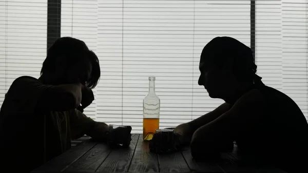 フレームには2人の若者がカフェのテーブルに座っている 彼らは何かについて話している 人は飲み物を持っていて 味が好きではない もう一人は彼を見ている アルコール依存症を示す — ストック写真