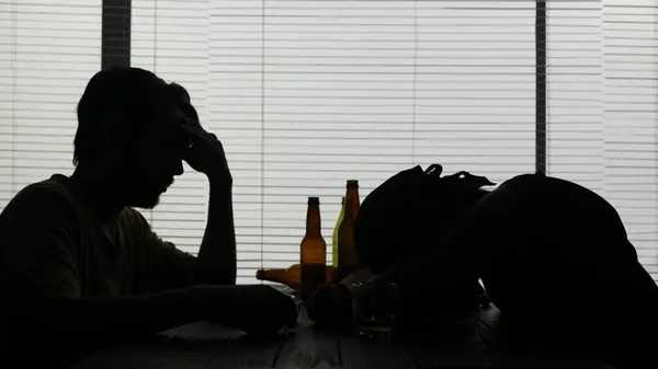 2人の男がカフェのテーブルに座っている 彼らは空のボトルの隣に座り 彼らはたくさん飲んだ 一人の男がテーブルで眠り 二人目の男が座って悲しんでいる アルコール依存症のデモ メディア — ストック写真