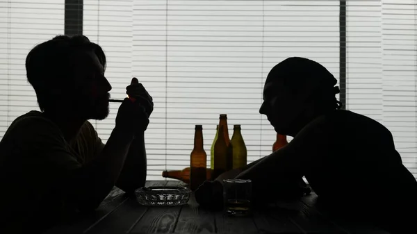 建物のテーブルに座っている若者たち 空のボトルに囲まれている 一人の男がタバコを灯している もう一人は目覚め アルコールを終えました もう一人は寝ていると話す — ストック写真