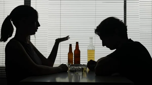 男と女が周囲のボトルのテーブルに座っている テーブルの上のワイングラスには アルコールがかかります 彼がアルコールを飲む喧嘩を告発する 女性はタバコを点灯し 彼と一緒に言った — ストック写真