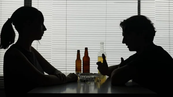 男と女が周囲のボトルのテーブルに座っている テーブルの上のワイングラスには アルコールがかかります 彼がアルコールを飲む喧嘩を告発する 女性はタバコを点灯し 彼と一緒に言った — ストック写真