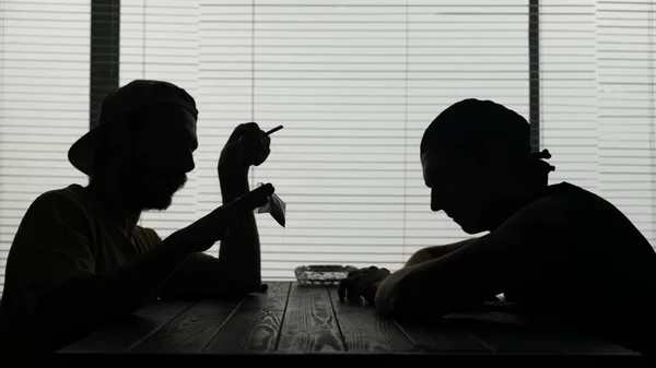 この映像は カフェのテーブルに座っている2人の若者を映している 一つは 喫煙して麻薬の袋を持っています 彼らは取引のために会った 彼らは何かについて話し バッグを見ます — ストック写真
