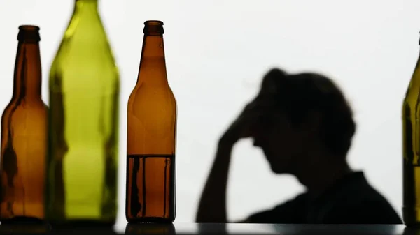 In the close up shot, there are empty, broken glass bottles full of alcohol. In the background, the man is strong he is very sad, sad, sad. Demonstrates the struggle with addiction. Medium shot.