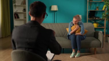 Erkek bir psikolog depresyondan muzdarip mutsuz bir kadınla çalışıyor. Kadın, uzmanın önünde kanepede oturur ve yastığa sarılır. Psikoterapi seansına katılacağım.