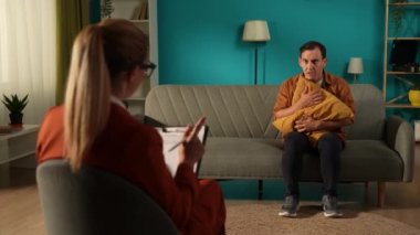 Depresyondan muzdarip mutsuz bir adamla çalışan bir kadın psikolog. Bir adam bir uzmanın önünde kanepede oturuyor, yastığa sarılıyor. Ruh sağlığı, depresyon, panik atak kavramı