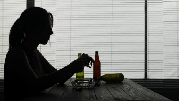 フレームには 若い女性が空のボトルに囲まれたテーブルの上に座っています 彼女はアルコール中毒を示している 彼女はタバコを拾い ライトをつけ それを吸う 悲しい イライラ — ストック動画