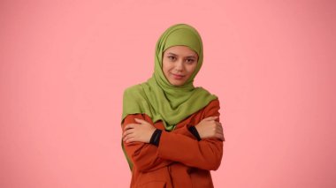 Orta boy izole bir fotoğraf, tesettürlü, duvak takan çekici bir genç kadın. Kendini kucaklıyor, hafifçe gülümsüyor, sevimli ve utangaç davranıyor. Reklamınıza, kültürünüze, çeşitliliğinize yer.