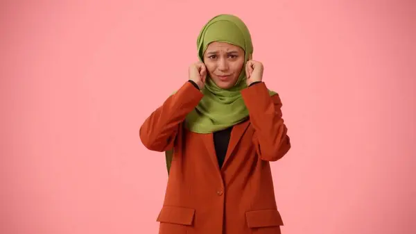 Medium-sized isolated photo capturing an attractive young woman wearing a hijab, veil. She is plugging her ears with fingers in disagreement. Place for your advertisement, cultural, diversity.