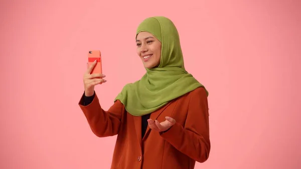 Medium-sized isolated photo capturing an attractive young woman wearing a hijab, veil. She is recording herself, having a videocall and talking actively. Place for advertisement, cultural, diversity.