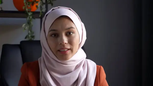 Close up photo capturing an attractive young woman in a hijab, veil sitting in the room or office. She is speaking to the camera, relaxed and confident. Cultural diversity, inclusivity, advertisement.