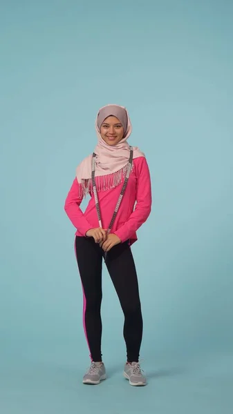 Full-sized isolated photo capturing an attractive young woman wearing a sportswear and a hijab, sheila. She hung a tape measure around her neck. Place for advertisement, promotional, loosing weight.