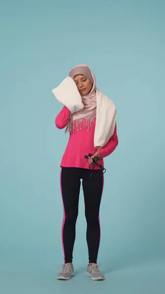 スポーツウェアとヒジャーブで若い女性を撮影するフルサイズの孤立した写真 シラは 運動した後 ジャンプロープを保持し 額から汗を拭きます プロモーション スポーツのための場所 — ストック写真