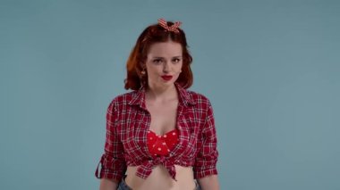 Mavi arkaplanda parlak makyajlı genç bir kadın var. Kameraya bakıyor ve hiçbir şeyi inkar etmiyor. Kafasını hiç hoşlanmadığı bir şeyle sallıyor. Hoşnutsuzluğu, olumsuzluğu göster.