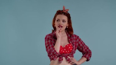 Mavi arkaplanda parlak makyajlı kızıl saçlı genç bir kız var. O chupa chup yiyor ve bir şeyler düşünüyor, düşünüyor, rüya görüyor. Sonra utanarak kameraya baktı.