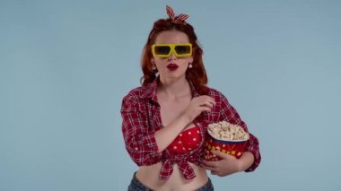 Mavi arkaplanda, parlak makyajlı kızıl saçlı genç bir kadın var. Tiyatroda 3 boyutlu gözlüklü bir film izlediğini gösteriyor, şaşırdığını ifade ediyor. Orta boy video.