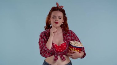Mavi arkaplanda, parlak makyajlı kızıl saçlı genç bir kadın var. Tiyatroda film izlediğini gösteriyor. Dikkatle izliyor, elinde patlamış mısırla, konsantre. Orta boy video.