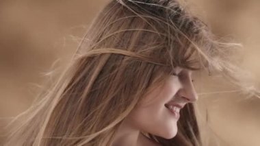 Beyaz saçlı genç bir kadının yakın çekimi. Kafasını farklı yönlere çeviriyor, rüzgar ona esiyor. O, elleriyle saçlarını tarar ve gülümseyerek yüzünü uzaklaştırır. Yavaş çekim.