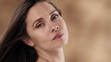 Çerçevede orta yaşlı bir kadın var. O yan yana duruyor, yana bakıyor. Yavaşça başını çevirir, kameraya bakar ve gülümser. Rüzgar saçlarını savuruyor. Yavaş çekim.