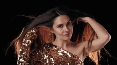 Siyah arka planda, orta yaşlı, siyah saçlı bir kadın. Rüzgar onun üzerine esiyor ve ışık onun üzerine parlıyor. Başını farklı yönlere çevirir ve kameraya bakar..