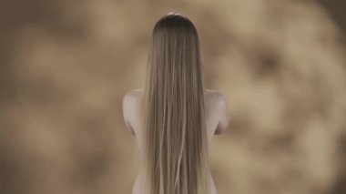Pürüzlü bir geçmişi olan genç bir kadın, uzun, beyaz ve kabarık saçlı. O, dış giysisi olmadan geride duruyor. Saçlarını savurur, kollarından aşağı düşer. Ağır çekim. HDR BT2020