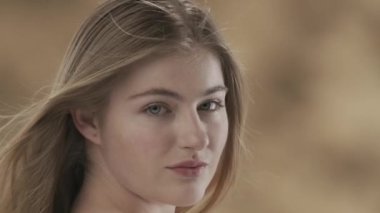 Üç renkli arka planda, uzun beyaz saçlı, güzel bir kadının yakın plan çekiminde. O, saçını yana doğru kamçılıyor. Kameraya bakar ve gülümser. Ağır çekim. HDR BT2020 HLG