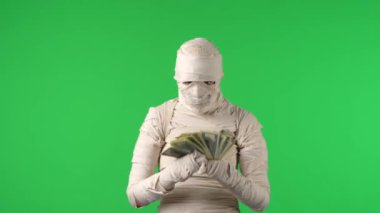 Yeşil ekran, bir mumya yakalayan kroma anahtarı videosu. Bir deste banknot, para gösteriyor ve havaya fırlatıyor. Cadılar Bayramı. Model yapın, tanıtım videonuz ya da reklamınız için çalışma alanı