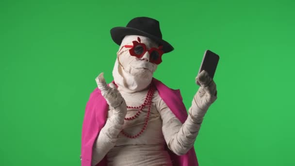 グリーンスクリーンは ピンクのジャケット セルフィーを着用しているミイラをキャプチャするクロマキービデオをスマートフォンで分離しました モックアップ プロモーションクリップや広告のためのワークスペース — ストック動画