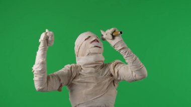 Yeşil ekran izole edilmiş kroma anahtar fotoğrafı bir mumyanın dans edişini çekiyor ve mikrofona şarkı söylüyor. Cadılar bayramı. Model yapın, tanıtım videonuz ya da reklamınız için çalışma alanı.