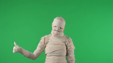 Yeşil ekran izole edilmiş kroma anahtar fotoğrafı bir mumyanın eliyle bir şey göstermesini ve baş parmağını kaldırmasını gösteriyor. Cadılar Bayramı. Model yapın, tanıtım videonuz ya da ürün reklamınız için çalışma alanı