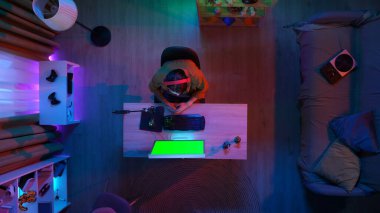 Oyun ve yayın konsepti. Kulaklıklı erkek, odada oturmuş Chroma anahtar yeşil ekranlı monitöre bakıyor. Reklam alanı çalışma alanı modeli..