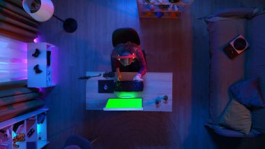 Oyun ve yayın konsepti. Kulaklıklı bir kızın odada oturmuş el salladığı fotoğraf makinesi, Chroma 'lı bilgisayar yeşil ekran, reklam alanı çalışma alanı modeli..