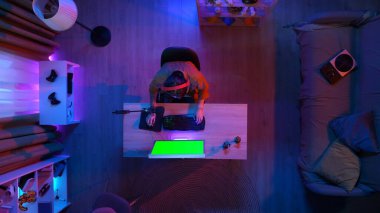 Oyun ve yayın konsepti. Kulaklıklı erkek, odada masada oturmuş bilgisayar başında Chroma anahtar yeşil ekran, reklam alanı çalışma alanı modeli ile oyun oynuyor..