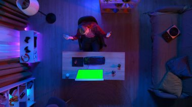 Oyun ve yayın konsepti. En iyi görüntü, odada masada oturan kızın bilgisayarla oyun oynaması Chroma tuşlu yeşil ekranla, kazanan bir jest. reklam alanı çalışma alanı modeli.