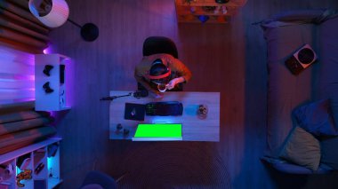 Oyun ve yayın konsepti. Kulaklıklı erkek, odada oturmuş PC 'ye bakıyor kahve içiyor, Krom yeşil ekranlı monitör, reklam alanının çalışma alanı modelini yapıyor..