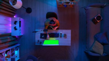 Oyun ve yayın konsepti. Kulaklıklı erkek, odada masada oturmuş bilgisayarın atıştırmalık yemesine bakıyor, Chroma 'nın yeşil ekranını izliyor, reklam alanının çalışma alanı modelini yapıyor..