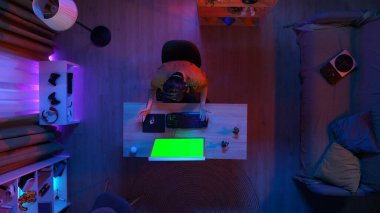 Oyun ve yayın konsepti. Kulaklık takan erkek, odada masada oturmuş PC 'ye bakıyor, Krom anahtar yeşil ekran, reklam alanı çalışma alanı modellemesi yapıyor..