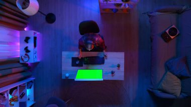 Oyun ve yayın konsepti. Kulaklık takmış bir kadının odadaki masada oturup PC 'ye bakması, Krom anahtar yeşil ekran, reklam alanı çalışma alanı modellemesi..