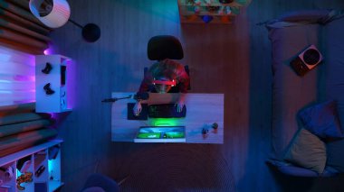 Çevrimiçi oyun reklam konsepti. Bilgisayardaki odadaki kızın portresi. Masada oturan kulaklıklı kadının üst görüntüsü, elleri klavyede, çevrimiçi bilgisayarda oyun oynuyor ve yayın yapıyor..