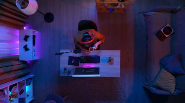 Çevrimiçi oyun reklam konsepti. Evde modern bilgisayar olan bir oda manzarası. Kulaklıklı bir adamın internette oyun oynaması, abur cubur yemesi, kahve içmesi..