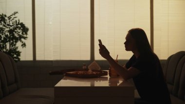 Günlük hayat ve insan ilişkileri kavramı. Kafeteryadaki kişinin portresi. Barda oturan, elinde akıllı telefonuyla sosyal medyada haber okuyan genç bir kadının silueti..