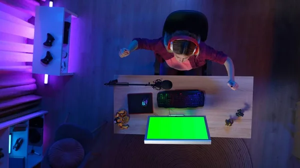 Gaming and streaming advertisement concept. Person on the PC at home. Top view of woman at the computer with Chroma key green screen, won the mission in the game, advertising area workspace mockup.